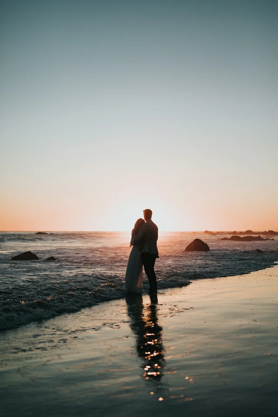A couple standing together on the beach at sunset