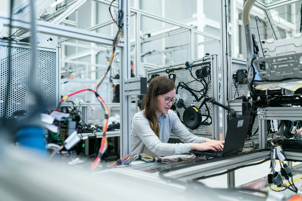 A project specialist working from a laptop inside a manufacturing facility