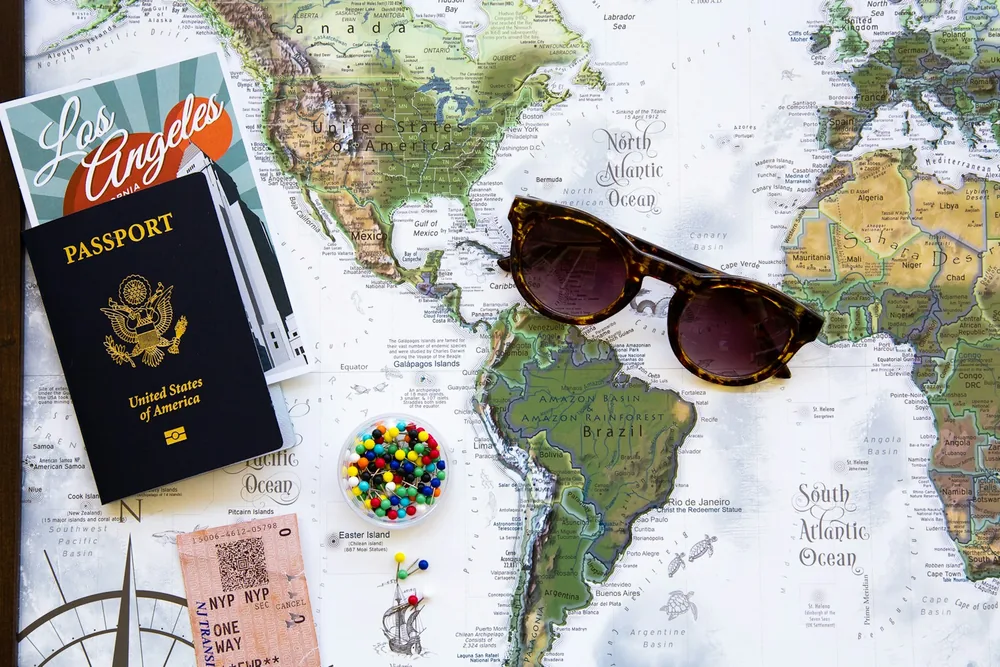 A passport, map, sunglasses, and travel pins arranged for itinerary planning